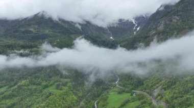 Bulutların arasından İHA uçuşu. İtalya 'daki Alp Dağları manzarası. Yeşil dağlar, vadilerin üzerindeki bulutlar