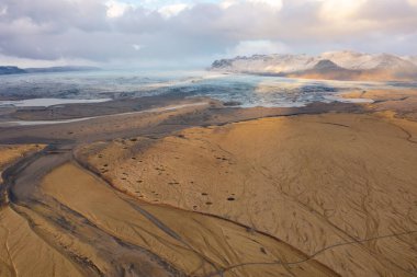Cloudy sunset drone view mountain peaks covered with snow. Volcanic valley below. East Iceland. clipart