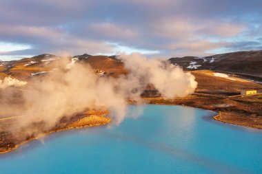 Bulutların arasından geçen drone görüntüleri engebeli arazi ve dağlarla mavi göl. İzlanda, Kuzeydoğu Bölgesi