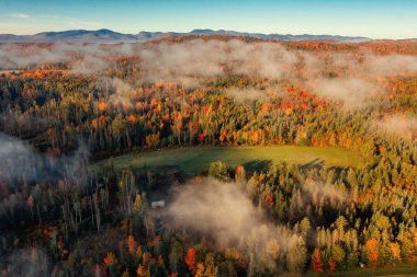 Sonbahar ormanı bulutların altındaki izole evi, dağ zeminini süslüyor. İHA görüntüsü. New Hampshire