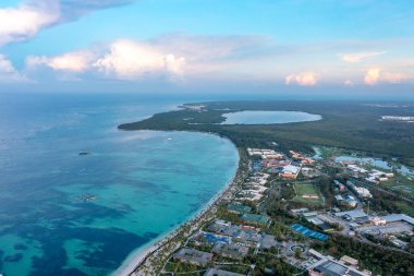 İnsansız hava aracı saman şemsiyeli, palmiye ağaçlı, otelli Atlantik tropikal plajını görüyor. Punta Cana, Dominicana