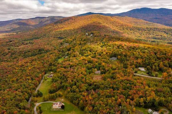 Sonbahar ormanı, bulutların altındaki köyü arka plan dağlarına karşı süsler. Drone fotoğrafı. Vermont, ABD