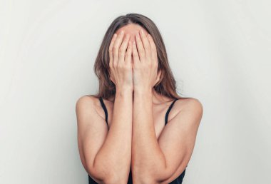 Elleriyle yüzünü kapatan kadın korku, acı ve hayal kırıklığı hisseder. Baş ağrısı kavramı