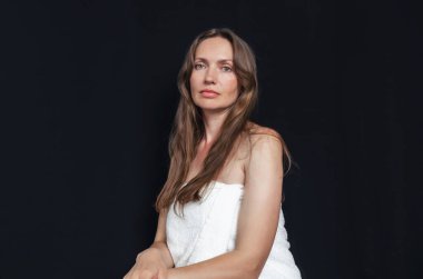 Siyah arka planda beyaz bir havluya sarılı uzun saçlı çekici orta yaşlı kadın portresi.