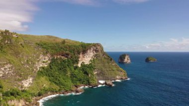 Nusa Penida, Endonezya. Mavi deniz, ormanla kaplı kayalık dağları yıkar. Dinlenme ve seyahat kavramı