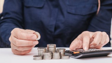 Koyu renk elbiseli bir kadın para biriktirir, hesap makinesinden kazanç hesaplar.