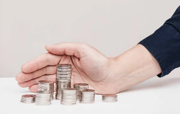 stock image Woman hand covers a stack of silver coins with her palm on a white table