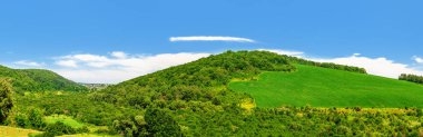 Yeşil çimen tepelerinin panoramik doğa manzarası ve kıvrımlı ufuk çizgisi olan mavi gökyüzü. Idyll.