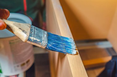 Marangoz, marangozluk atölyesinde fırçayla bir tahtanın yüzeyine yapıştırıcı sürer.