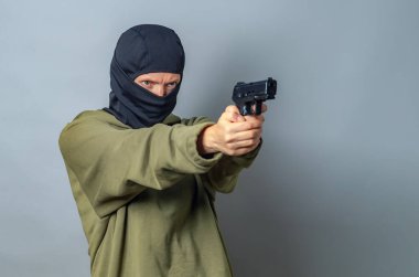 Kafasında kar maskesi olan kadın elinde silah tutuyor, sağa nişan alıyor. Gri arka plan. Boşluğu kopyala