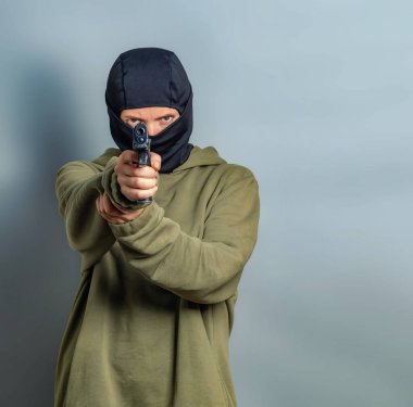 Siyah kar maskeli tehlikeli bir kadın haki kapüşonlu bir kapüşonlu giyiyor ve kameraya nişan alıyor. Gri arkaplan