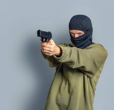 Kafasında kar maskesi olan kadın elinde silah tutuyor, sola nişan alıyor. Gri arka plan. Boşluğu kopyala