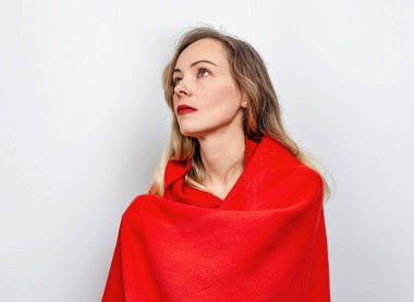 Omuzlarına sarılmış kırmızı pelerinli sakin sarışın portresi. Yukarı bak. Gri arkaplan