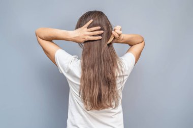 Uzun saçlarla savaşıyor. Beyaz tişörtlü kadın. Ellerini başının arkasına koy. Gri arkaplanda arka görünüm izole edildi