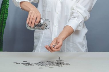 Beyaz gömlekli kadın cam kavanozdan avuç içine bozuk para döküyor. Mali giderler kavramı