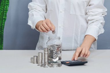 Beyaz gömlekli kadın bozuk para sayıyor. Cam kavanozdaki paraları sayıyorum. Tasarruf ve mali planlama kavramı