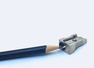 Keskinleştirilmiş siyah kalem metal açacağının yanında yatıyor. Beyaz arka plan, izole. Kırtasiye