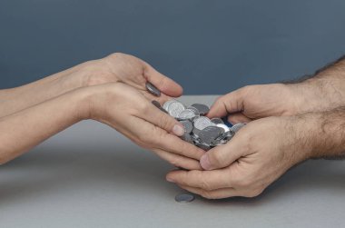 Parayı kişiden kişiye aktarın. Kadın eli, gümüş paraları erkeğin ellerine aktarır. Gri arkaplan