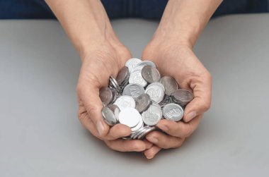 Dişi avuçlar gümüş para yığınını tutuyor. Kurumsal çevre iş dünyası. Gri stüdyo geçmişi