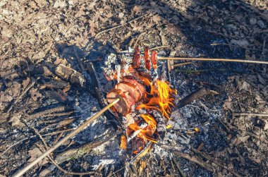 Et ve sosisler ormanda kamp ateşinde şişte kızarıyor.
