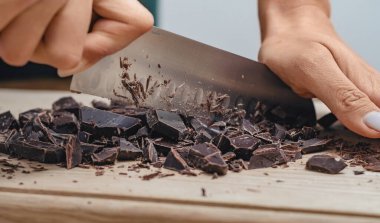 Tahta yüzeyde siyah çikolata doğrayan bıçak.