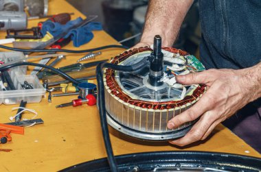 Tamir için elektrikli bisiklet motorunun yakın çekimi kaldırılıyor. Arkaplanda araçları olan tablo