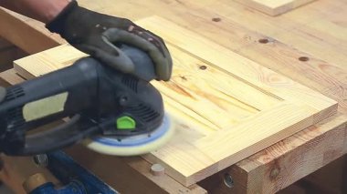 Marangoz, bir marangoz atölyesinde elektrikli zımpara makinesi kullanarak ahşap bir kapıyı zımparalıyor.