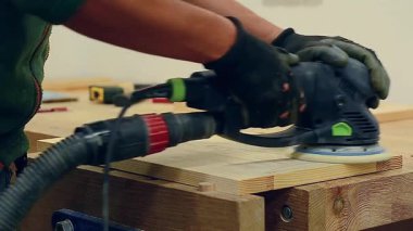 Marangoz, bir marangoz atölyesinde elektrikli zımpara makinesi kullanarak ahşap bir kapıyı zımparalıyor.