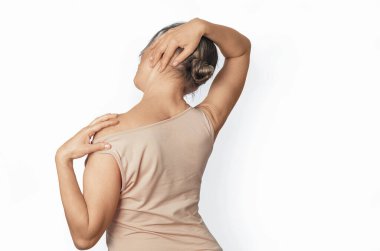 Çıplak omuzlu bej gömlekli kadın boyun kaslarını esnetiyor. Acıyı önlemek için başını sağa doğru eğiyor. Sağlık kavramı