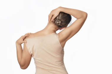 Bej gömlekli, çıplak omuzlu bir kadın boynu gevşetiyor, boyun kaslarını geriyor. Ağrıyı önlemek için başını sağa eğiyor.