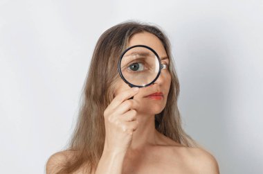 Büyüteçle büyüteçle uzun saçlı kadın kameraya büyük zoom gözüyle bakıyor, özgünlüğünü kontrol ediyor. Doğrulama, seçim kavramı