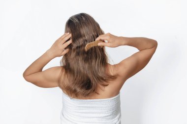 Beyaz havluyla omuzlarını açıp orta boyda saçlarını tarayan bir kadın. Duştan sonra sağlık ve bakım kavramı