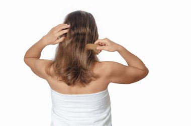 Çıplak omuzlu, beyaz arka planda ahşap tarakla orta saçlarını tarayan, izole edilmiş bir kadın..