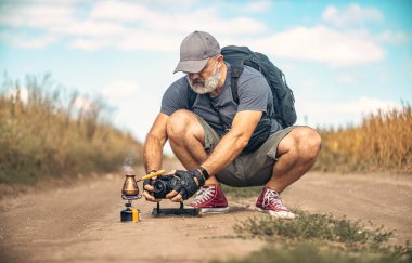 Erkek fotoğrafçı çömelmiş ve kamerayı tarla yolunun ortasında tutuyor. Türk kahve makinesinin fotoğraflarını çekiyor. Seyahat ve açık hava maceraları kavramı.