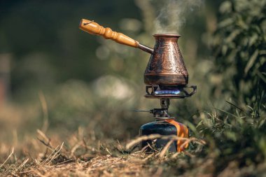 Kamp ateşinde Türk kahvesi kaynatıyorum. Mavi alevli ateş ve sıcak lezzetli kahvenin üstünde buhar. Lüks kamp konsepti.