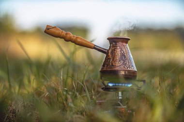 Çimenlerin arasında mavi alev bulunan gaz ocağına işlenmiş bakır işlemeli kahve buharı. Seçici odaklanma. Sabah kahve içme zamanı.