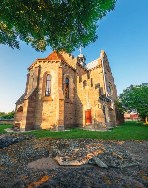 Aşağıdan, yeşil bahçeli köy kilisesinin yeşil dalları ve yakınındaki ağaçlar görünüyor. Antik dini binaların manzarası