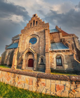Bulutlu gökyüzü altında eski bir kilise restore edildi. Kemerler, yarı dairesel pencereler, fayanslı çatı. Eski mimari
