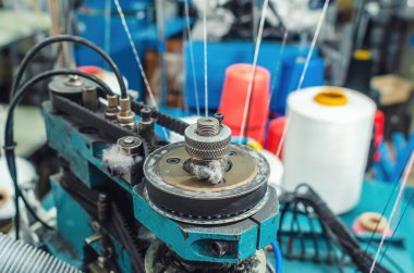 Tekstil endüstrisi, otomatik çorap örme. Renkli ipliklerin bulanık arka planında dairesel örgü makinesi