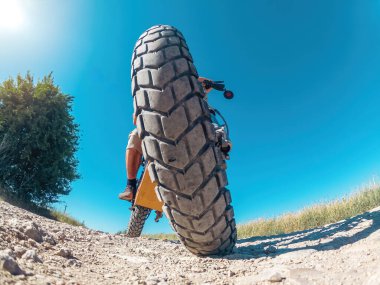 Düşük açılı, motorlu, yakınlaştırılmış elektrikli motosiklet tekerleğinin yaratıcı fotoğrafı. Mavi gökyüzü ile kavisli ufuk.