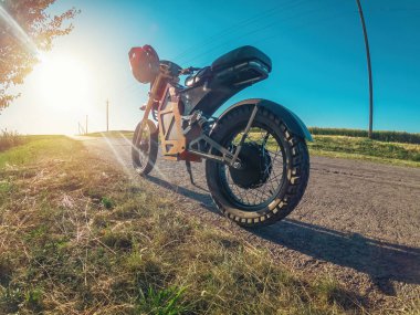 Elektrikli motosiklet yol kenarında, güneşin altında ağacın yanında duruyor. Moped modern kişisel taşımacılık. Gün batımı.