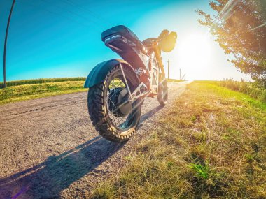 Elektrikli motosiklet yol kenarında, güneşin altında ağacın yanında duruyor. Moped modern kişisel taşımacılık. Gün batımı.
