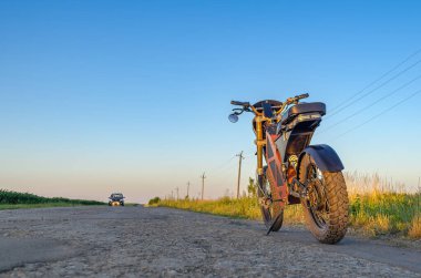 Elektrikli motosiklet kırsal yolun kenarında duruyor. Mavi gökyüzü arka planı. Modern çevre dostu ulaşım.