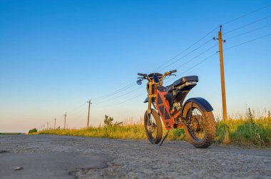 Elektrikli motosiklet kırsal yolun kenarında duruyor. Mavi gökyüzü arka planı. Modern çevre dostu ulaşım.