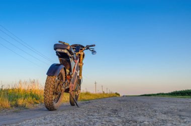 Elektrikli motosiklet kırsal yolun kenarında duruyor. Mavi gökyüzü arka planı. Modern çevre dostu ulaşım.