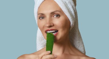 Yumuşak mavi arka planda mutlu bir kadının portresi elinde aloe vera tutarak beyaz dişlerle ısırıyor. Yaşlanma önleyici bakım konsepti.