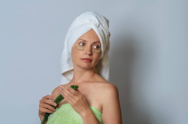 Doğal organik aloe vera bantları olan yetişkin bir kadın spa tedavileri, sağlık ve cilt bakımı için. Kafada havlu, ellerinde aloe yaprağı. Gri stüdyo geçmişi.