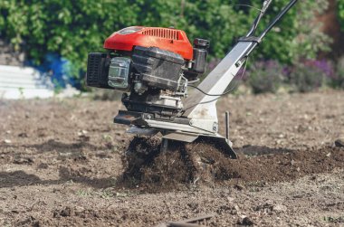 Elle benzin ekicisi toprağı sürer. Motor ekicinin pervanelerine yakın çekim. Toprak ekicinin altından uçup gidiyor. Çiftçilik kavramı.