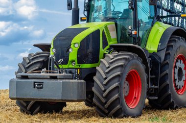 Modern traktör bulutlu gökyüzünün altında tarlada sakallı. Tarlalarda ve tarım endüstrisinde çalışma kavramı. Kapat..