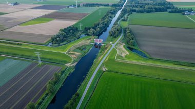 Köprü ile su kanalı. Hollanda 'daki su kanalının yanında tarım arazileri, tarlalar, elektrik direkleriyle çevrili ormanlar. Kırsal alan.